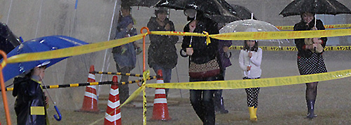 親子で傘を持って豪雨の中を歩いて体験している様子が8人ほど見えます