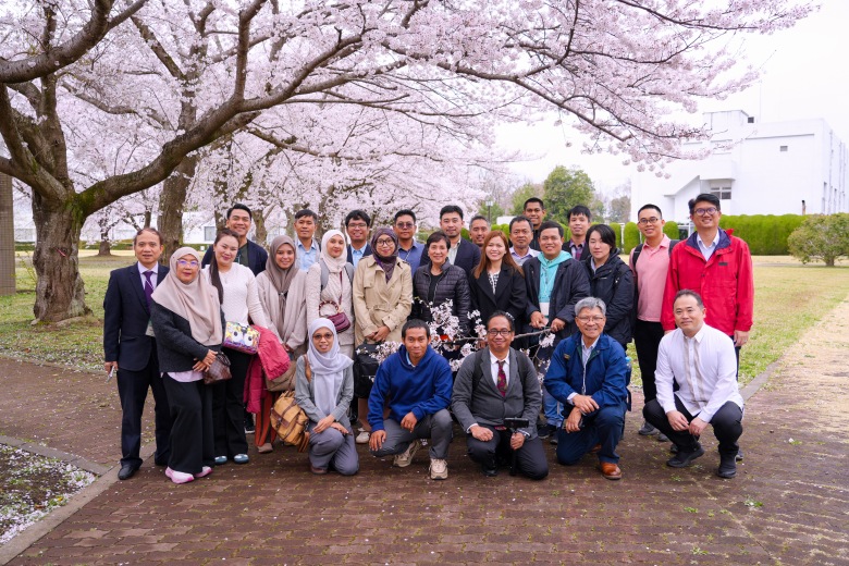  Participants visiting NIED and gathering under cherry blossoms during the facility tour.