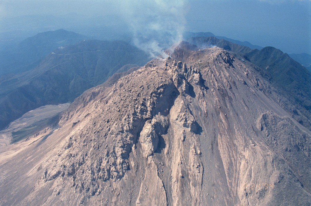 噴煙を上げる火山を上空から見た写真。火山の噴火によって山の形がつくられ、地球が今も活動していることがわかる。：写真