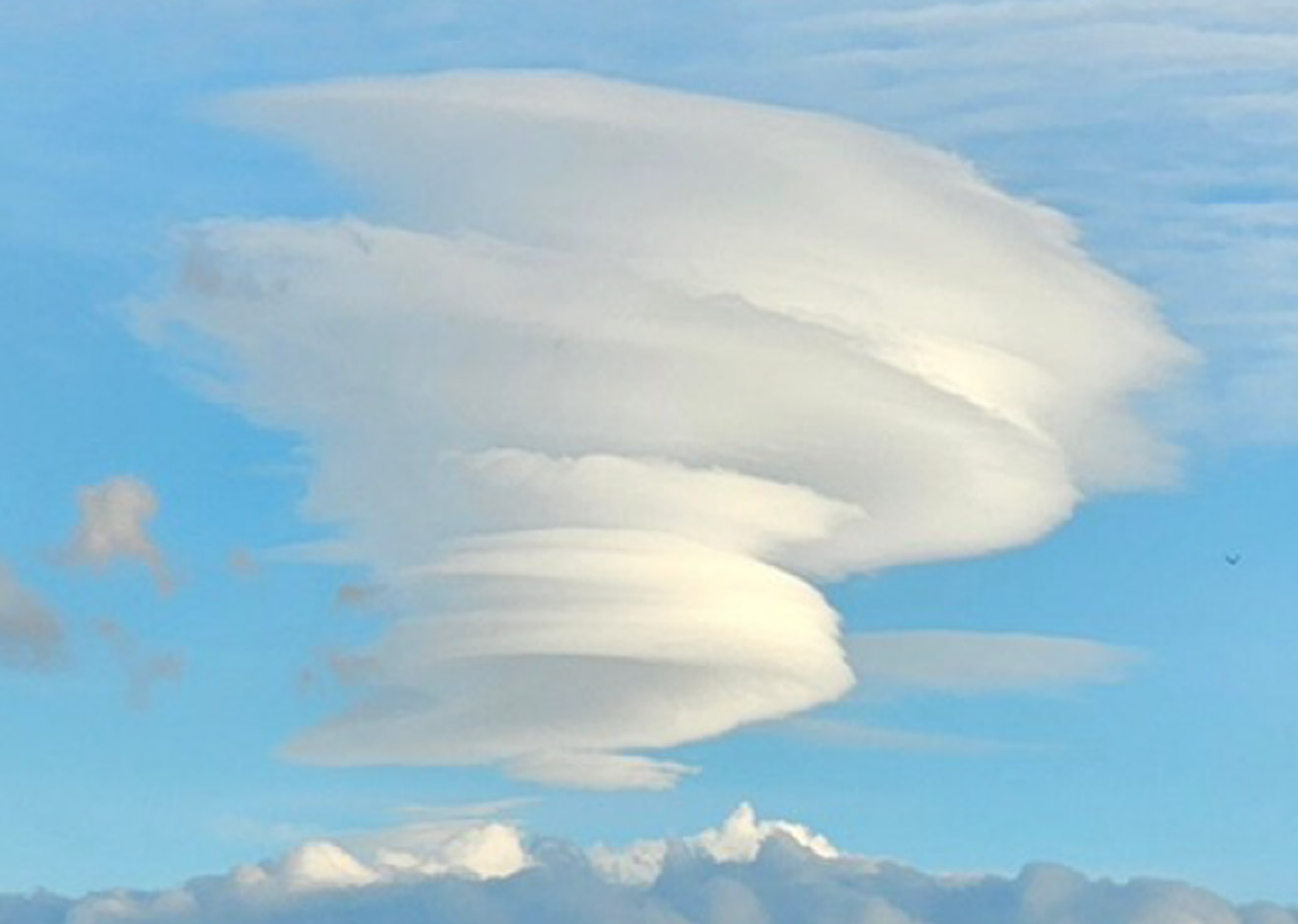 山の上空に、レンズのような形の雲が何層にも重なって見えるつるし雲。山の風下の同じ場所に止まっているように見える。：写真