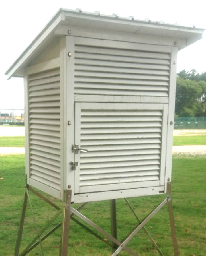 草地に設置された百葉箱。白いよろい戸のついた箱が金属の支柱の上にあり、直射日光をさえぎりながら気温や湿度を観測するために使われる。：写真