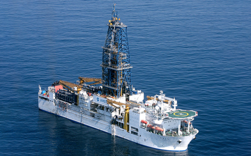 海底を掘削して地球内部を調べる、地球深部探査船「ちきゅう」。中央に高い掘削やぐらを備えた大型探査船が、海上に浮かんでいる。：写真